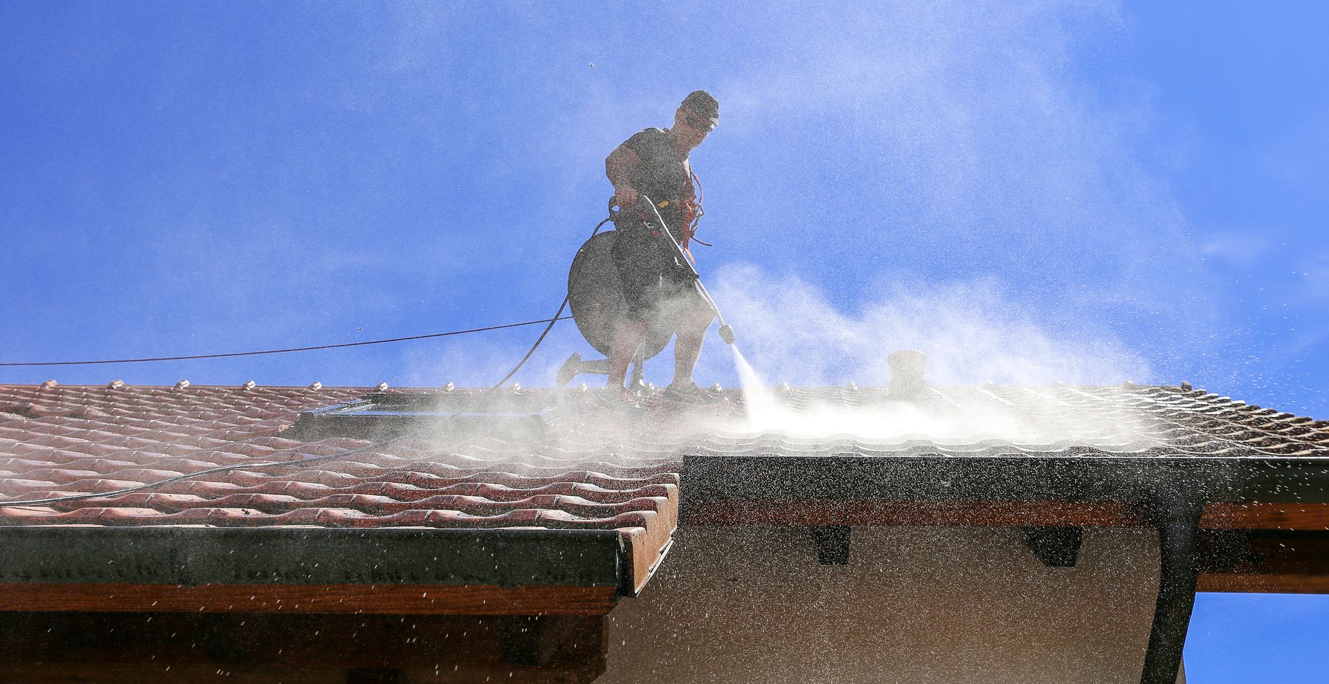 A man is cleaning the roof of a building with a soft pressure washer.