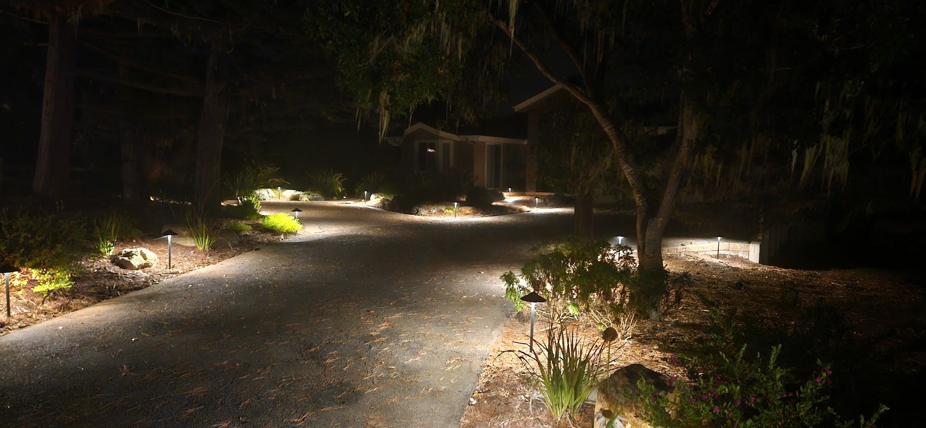 A driveway is lit up at night with a house in the background.