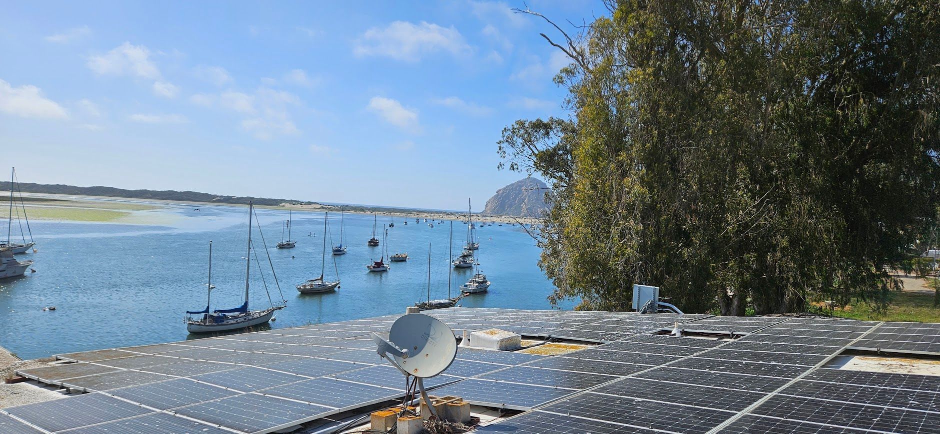 A satellite dish is sitting on top of a roof next to a body of water.