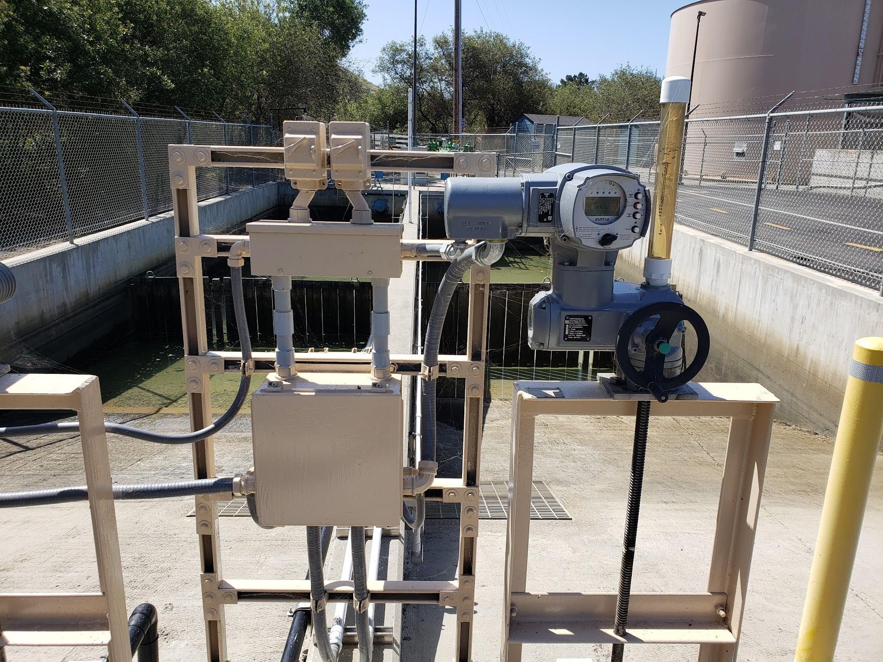 An industrial flow-monitoring instrument mounted on a metal frame above a water channel at an outdoor facility.