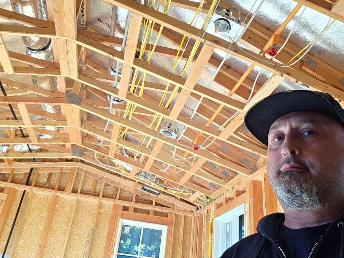 Man in black cap standing in unfinished room with exposed wooden rafters and insulation