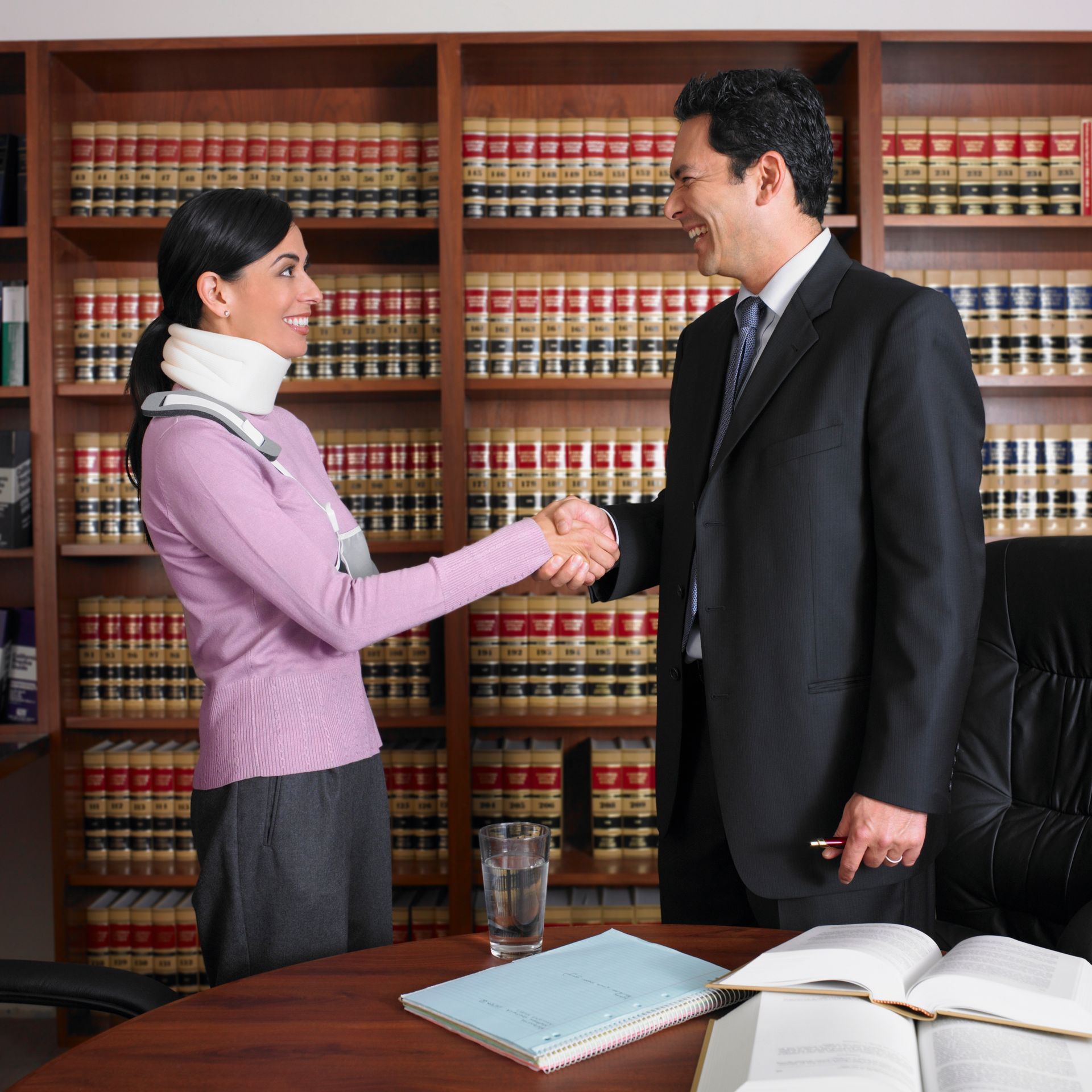 Woman with neck brace shakes hands with a lawyer in a law office with bookshelves.