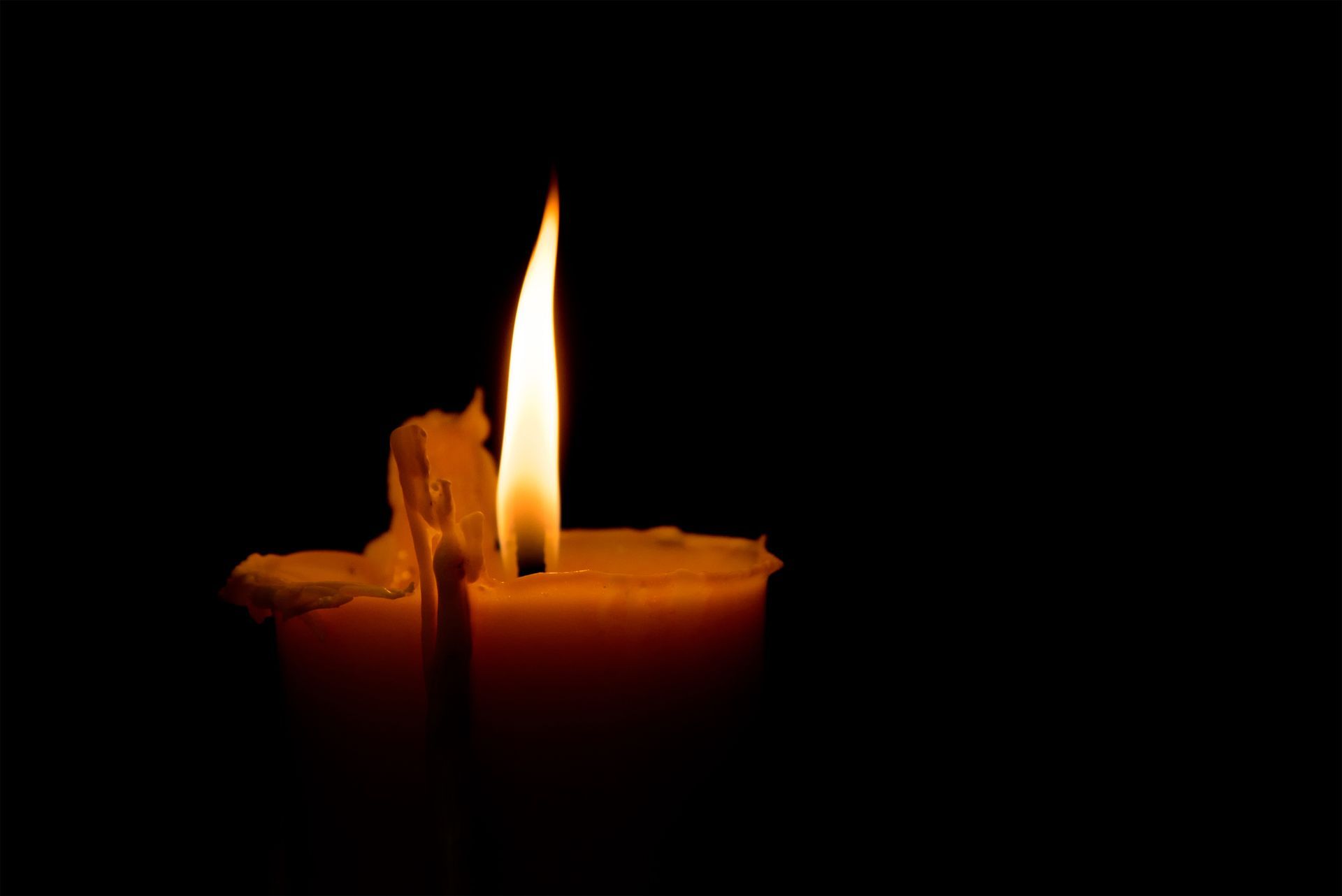 Candle burning in darkness, yellow flame with melted wax.