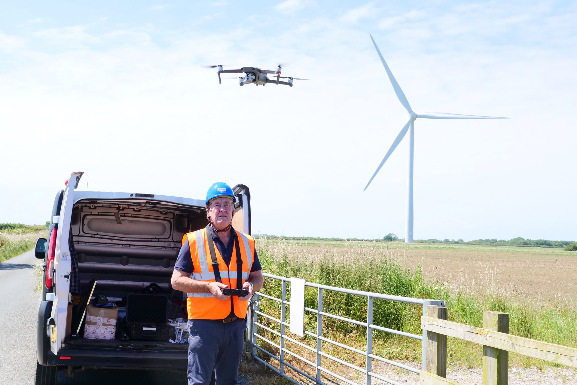 A man is standing next to a van with a drone flying in the background.