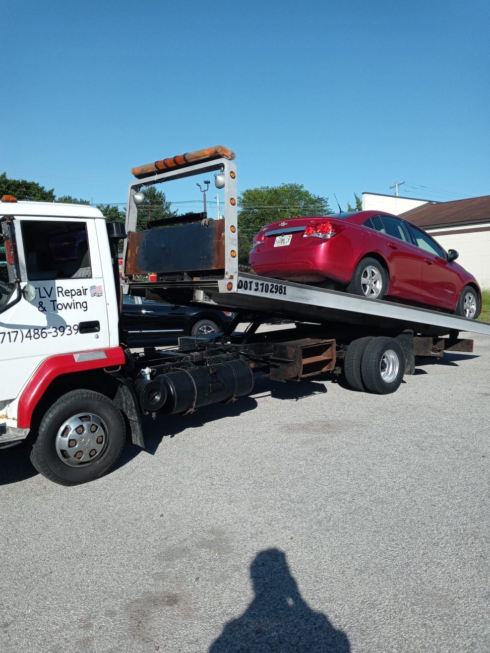 Tow truck carrying a red car on a sunny day.