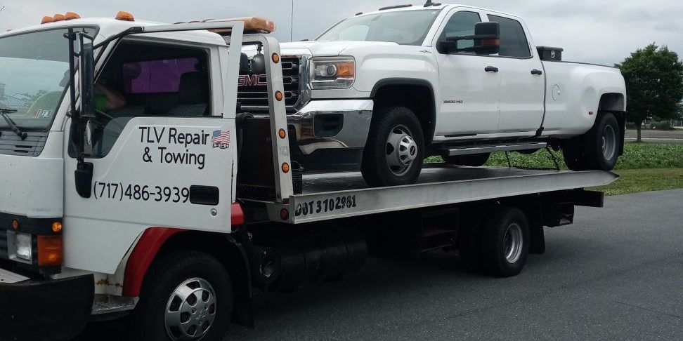 White tow truck carrying a white pickup truck. The truck is labeled 