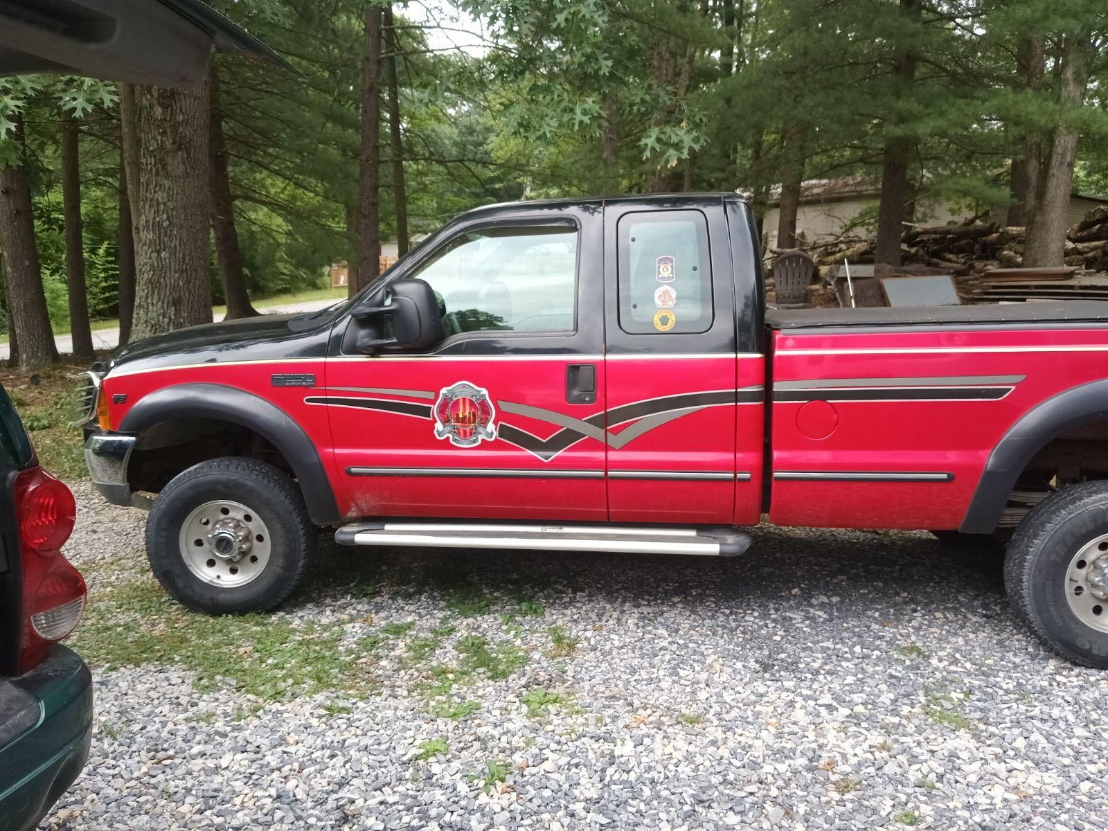 Red and black Ford truck parked on gravel, with a side step and decals.