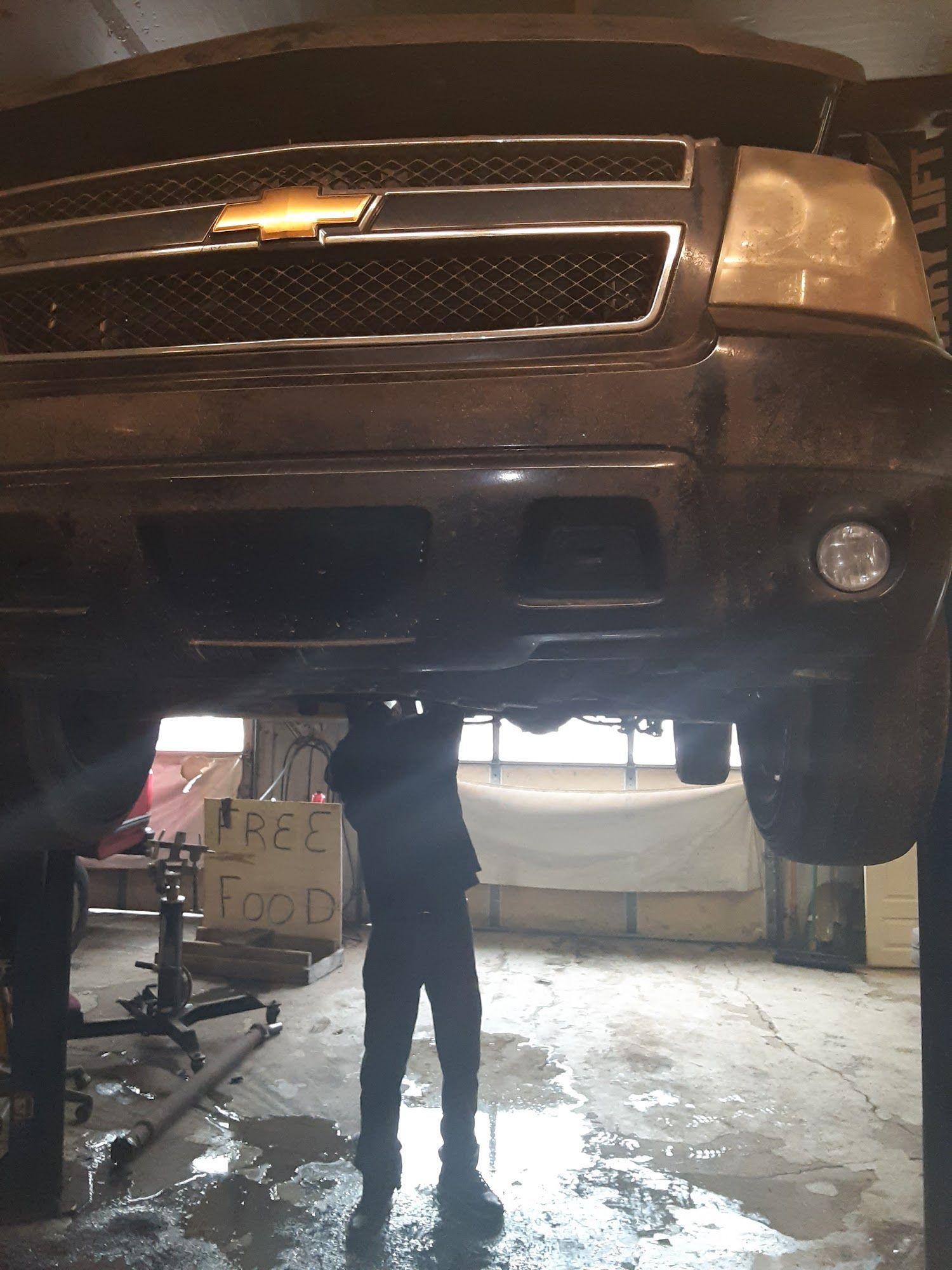 Person working under a black SUV lifted in a garage, with tools visible.