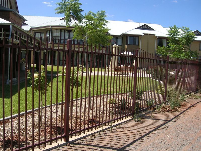 A fence surrounds a large house with a lawn in front of it