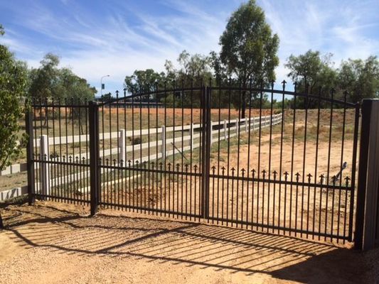 A black metal gate with a white fence in the background