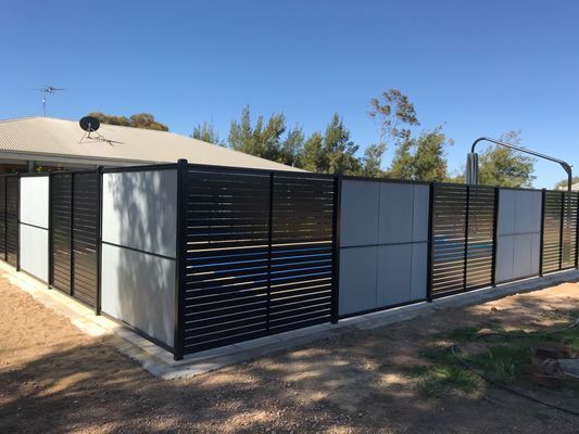 A black and white fence surrounds a swimming pool in front of a house.