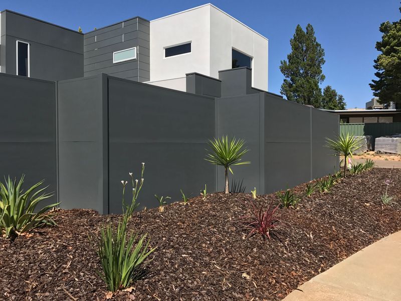 A fence surrounds a lush green garden in front of a house.
