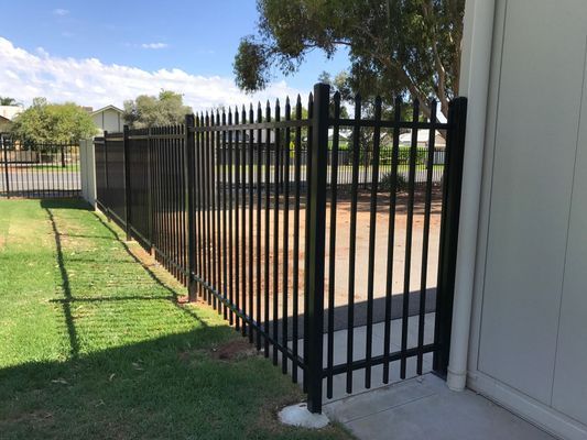 A black metal fence is surrounding a grassy area next to a garage.