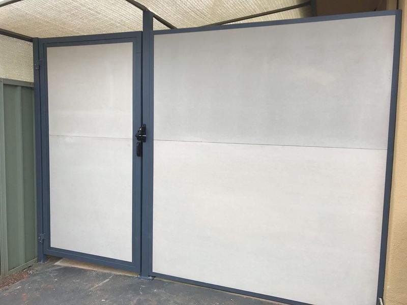 A white gate with a black handle is sitting next to a green fence.