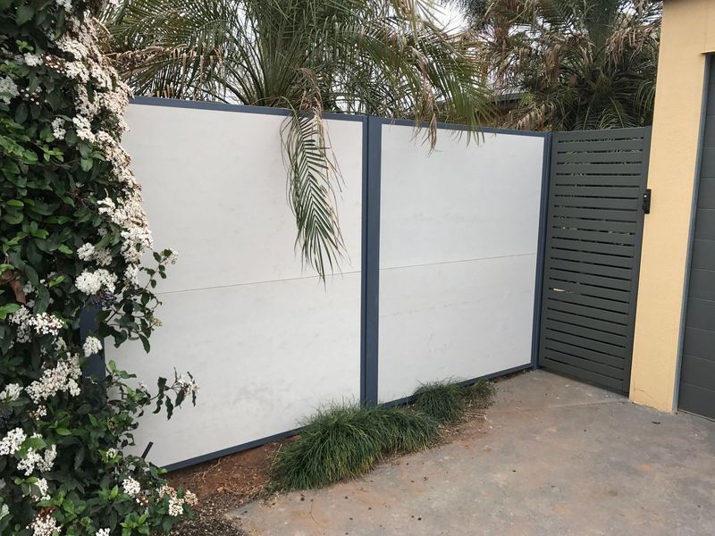 A white fence with a black trim is next to a bush with white flowers.