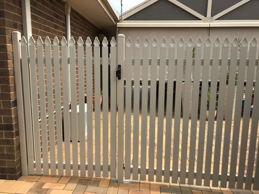 A white fence with a gate in front of a brick house.