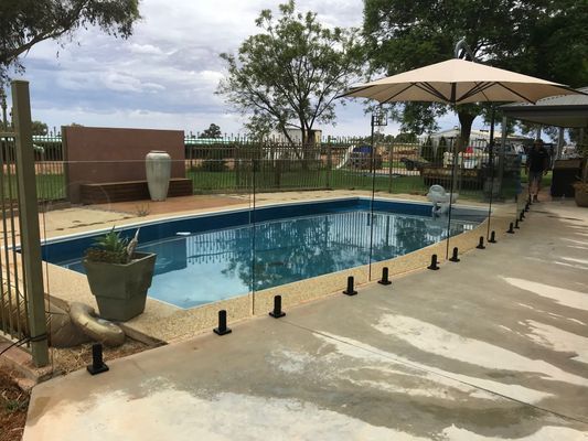 A large swimming pool with a fence and umbrella in the background.