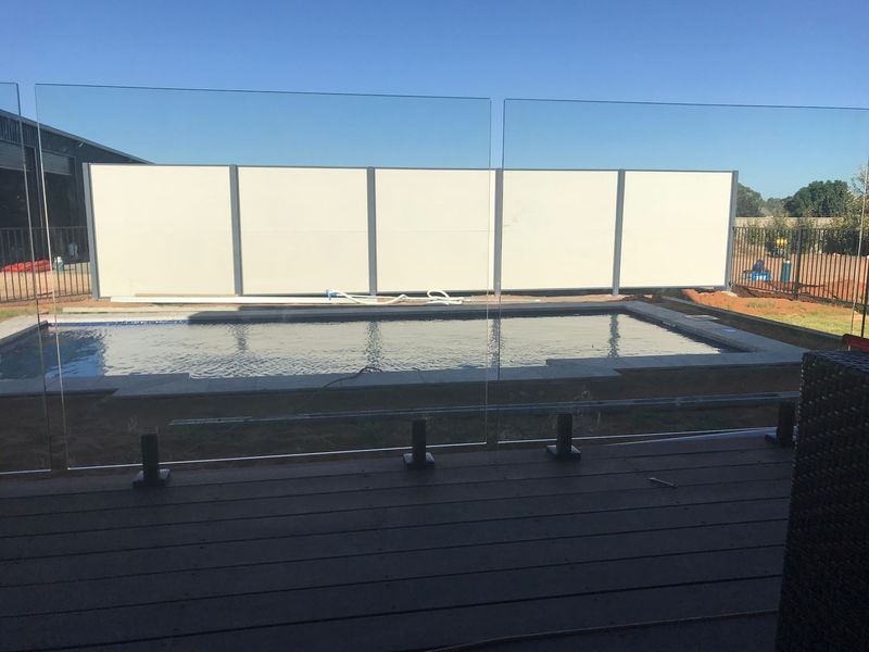 A large swimming pool is surrounded by a glass fence.