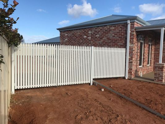 A white picket fence is in front of a brick house.