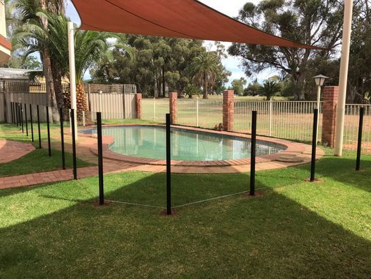 A swimming pool is surrounded by a fence and a shade sail.