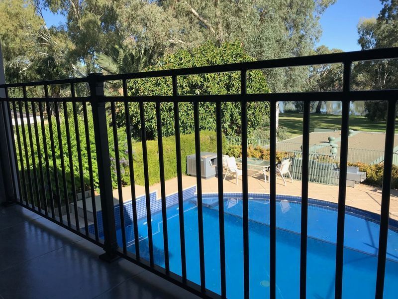 A balcony overlooking a swimming pool with a black railing.