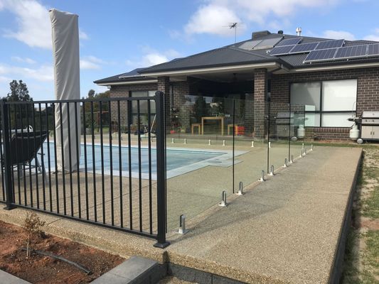 A fence surrounds a swimming pool in front of a house.