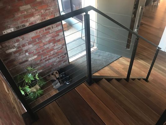 A wooden staircase with a black railing and a brick wall.