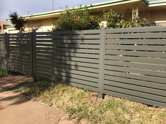 A wooden fence is surrounded by grass and bushes in front of a house.