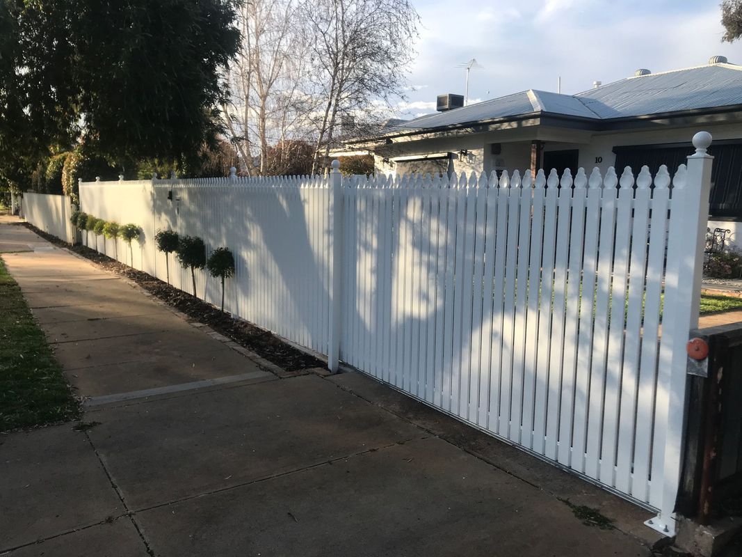 A white picket fence along a sidewalk next to a house.
