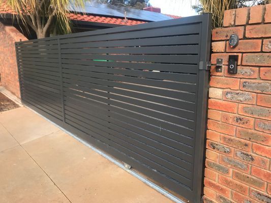 A black sliding gate is sitting next to a brick wall.