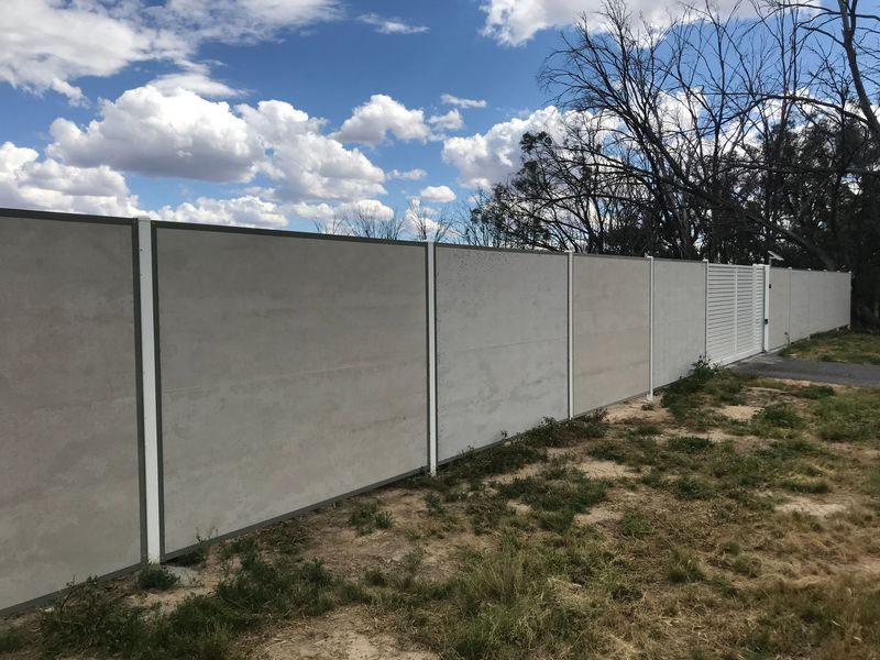 A concrete fence surrounds a grassy field with trees in the background.