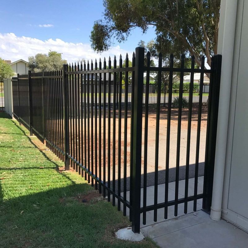 A black metal fence is surrounding a grassy area next to a building.