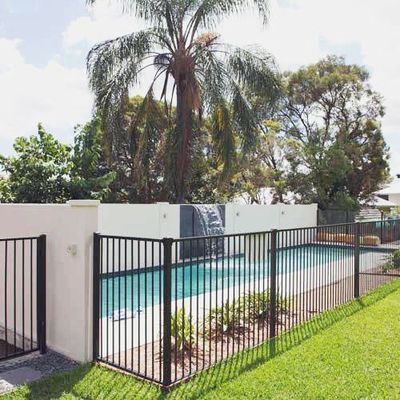A fence around a swimming pool with a waterfall in the background.