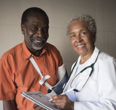 Man with arm sling and doctor in white coat smiling, looking at the camera.
