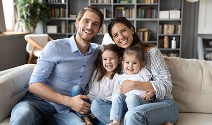 Family of four smiling on a couch in front of a bookshelf.