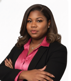 Woman in a black blazer and pink shirt, arms crossed, looking at the camera.