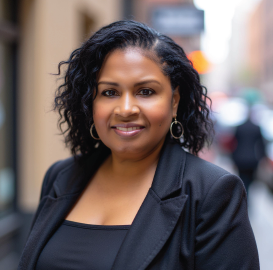 Woman in black blazer smiles, outdoors on a city street.