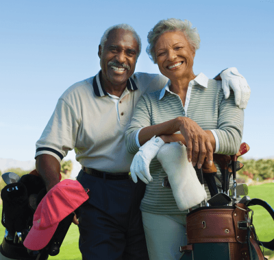 Smiling couple on a golf course, holding golf bags, posing outdoors on a sunny day.