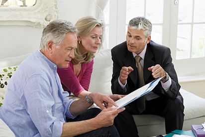 A man in a suit points at a document for a couple sitting on a couch.