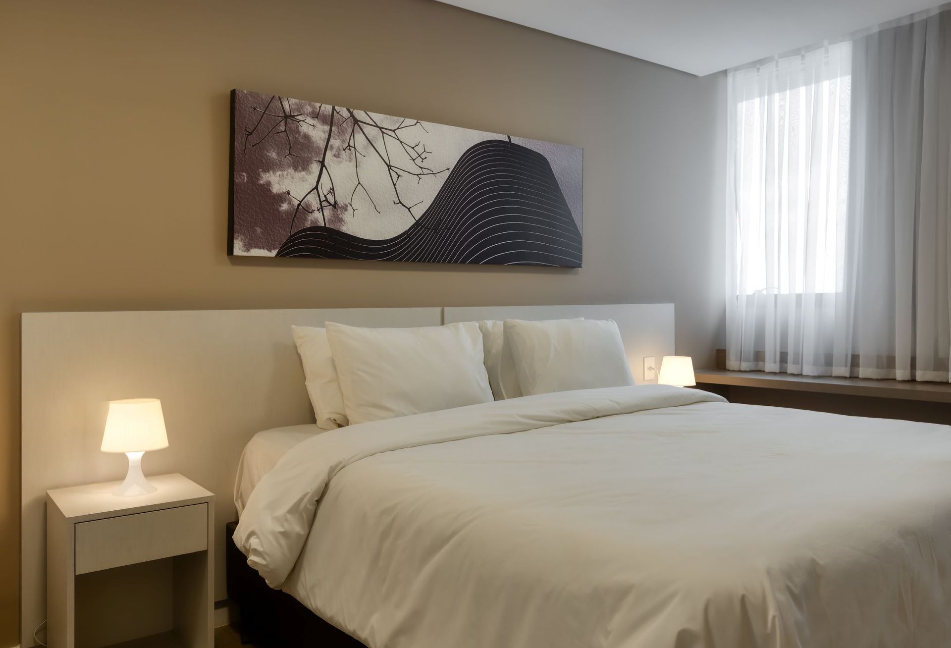 Um quarto de hotel com uma cama grande e uma pintura na parede acima dela.