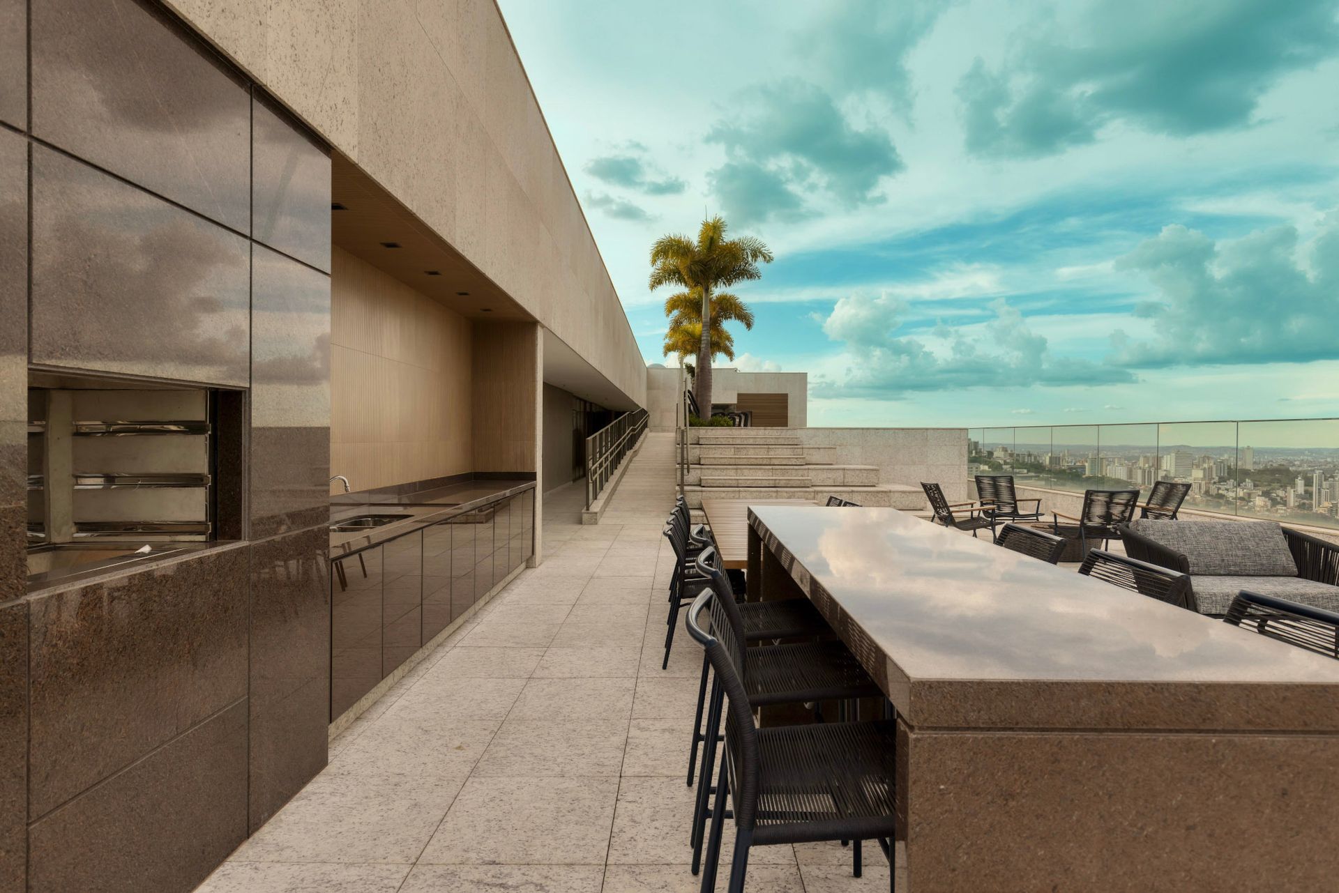 Uma grande mesa e cadeiras no terraço com uma palmeira ao fundo.