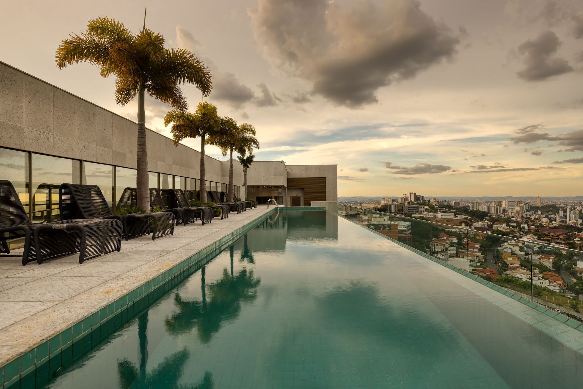 Uma piscina de borda infinita cercada por palmeiras e cadeiras com vista para a cidade.
