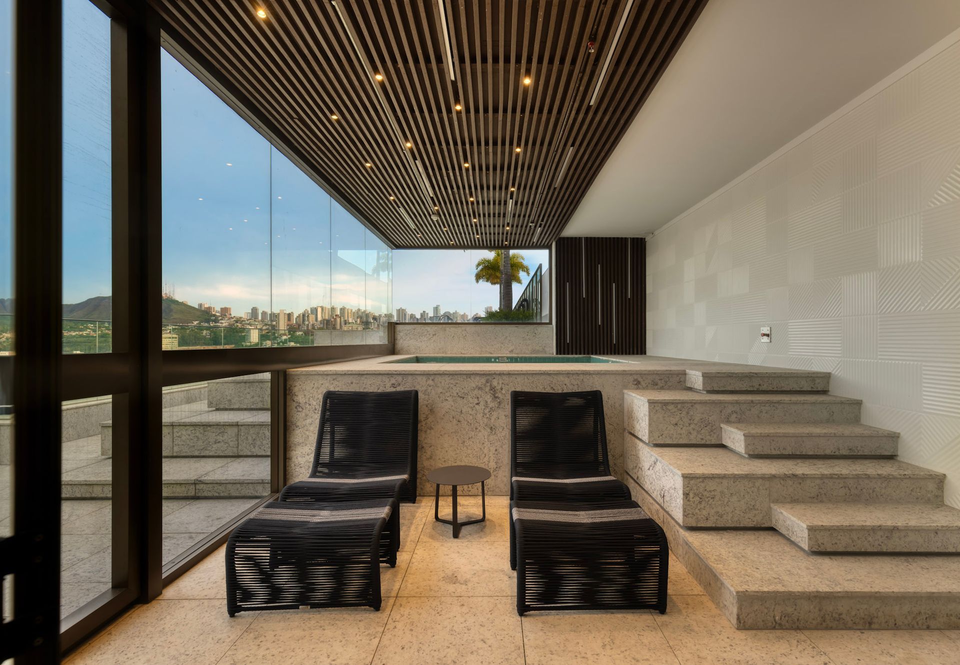 Uma sala com duas espreguiçadeiras e escadas que levam a uma banheira de hidromassagem.