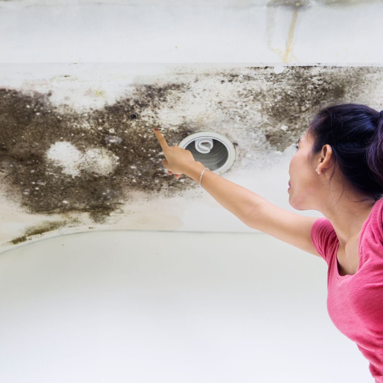 A woman in a pink shirt is pointing at a hole in the ceiling.