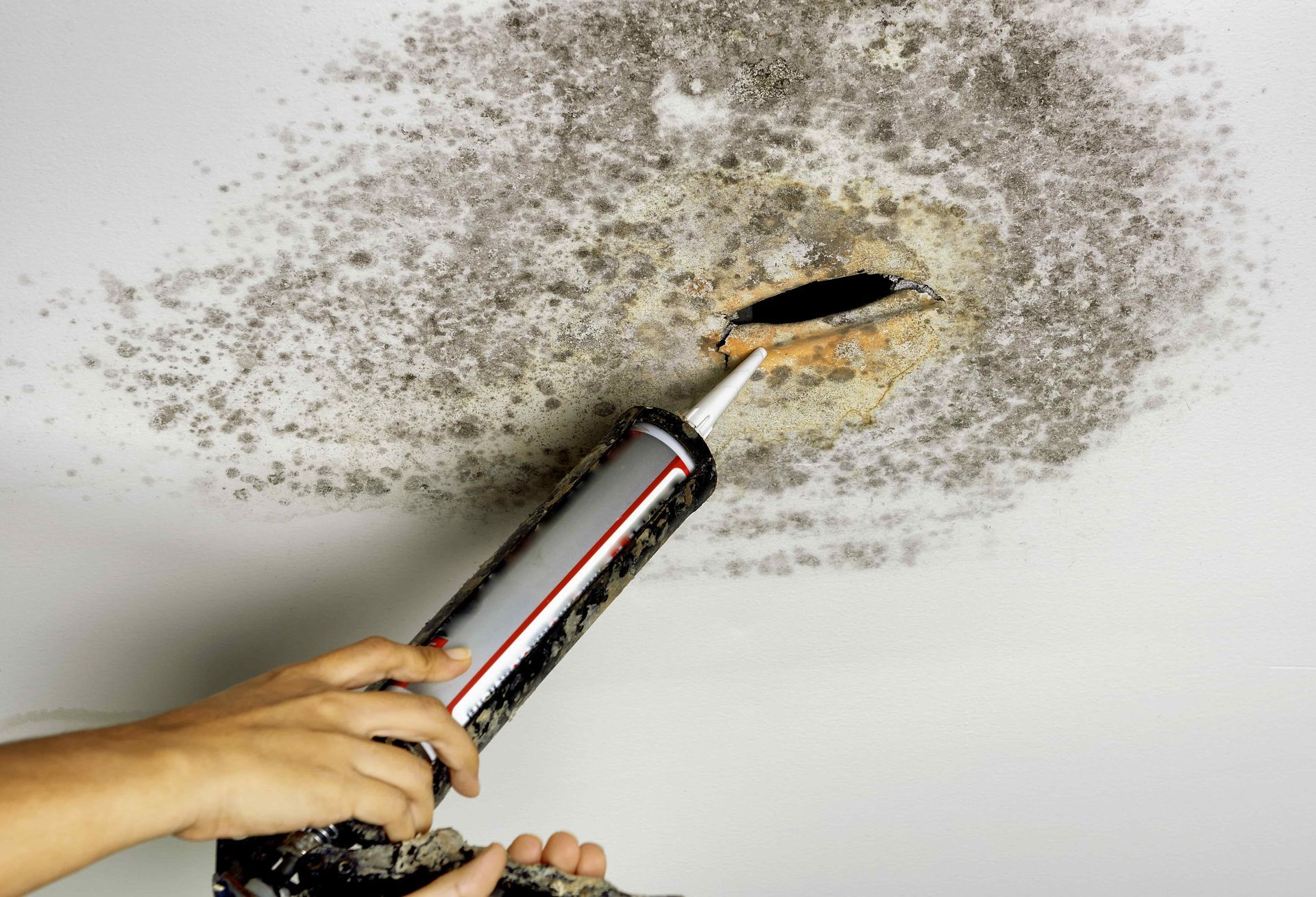 A person is applying silicone to a hole in the ceiling.