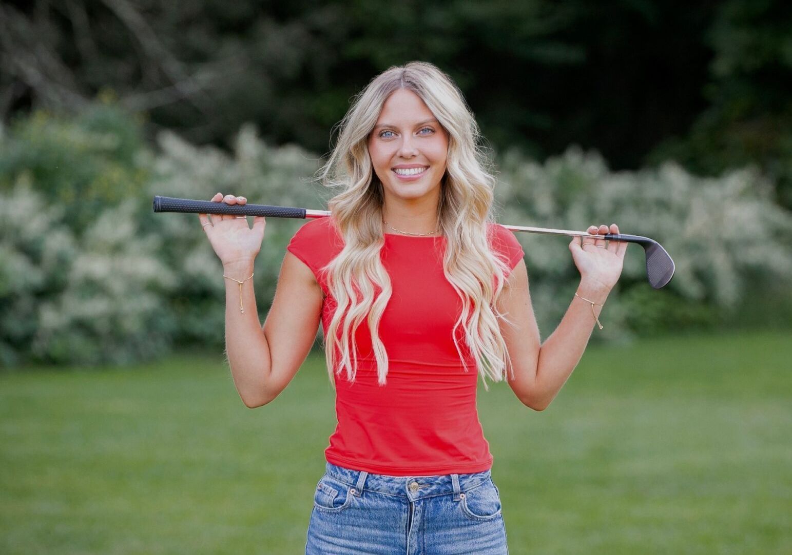 A woman in a red shirt is holding a golf club over her shoulder.