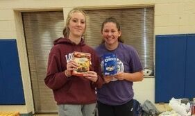 Two girls are standing next to each other holding boxes of cereal.
