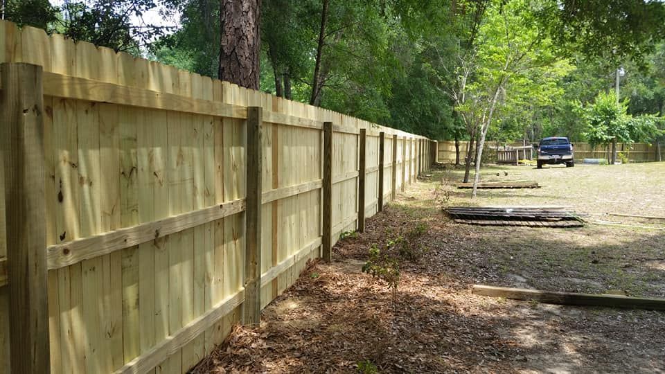 Wooden fence surrounding a grassy area with a vehicle parked in the distance.