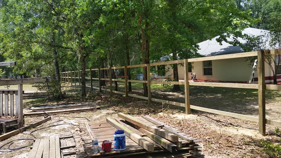 A wooden fence being built in a yard with a house and trees in the background.