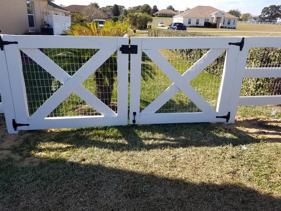 White wooden gate with X design, black hardware, set in grassy yard.